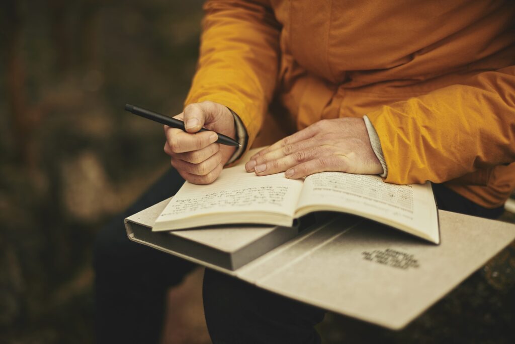 Bücher schreiben: Eine Frau mit gelbem Pullover schreibt in ein Tagebuch.
